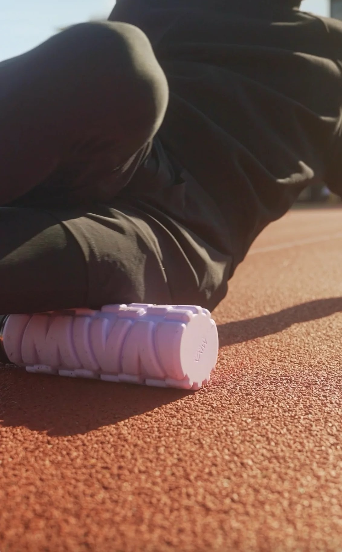 Runner foam rolls on a track using a MIVA Recovery foam roller and water bottle in one.