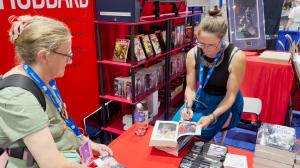 Illustrators of the Future 39 winner April Solomon signing a book for a lady at the Galaxy Press booth.