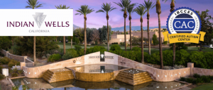 A scenic view of the Indian Wells entrance featuring palm trees, a water fountain, and a backdrop of mountains under a pink and purple sky.