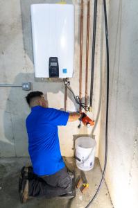 J. Blanton Plumbing technician installing a tankless water heater, highlighting the benefits of tankless water heaters, including efficient water heater installation and replacement services.