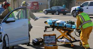 image of an open car door with firemen looking inside and another bringing a stretcher