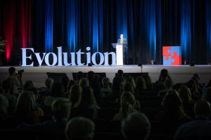 Man standing on stage at a conference with "Evolution" in big letters beside him