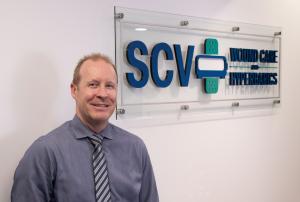 Founder & Medical Director, Ian R. Cook MD stands proud in front of a sign of the Santa Clarita Wound Care and Hyperbarics Logo.