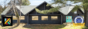 A cozy cabin with a wooden deck, two white chairs, and surrounded by tall trees and greenery.