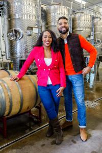 A man and a woman standing in front of stainless steel tanks used to make wine