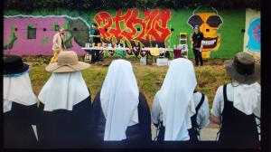 an image of five sisters (just the back of their heads) watching the artists paint a wall