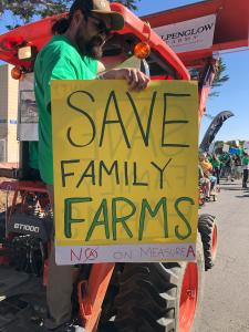 a man holding a sign at the Cannifest parade 2023 that says 'save family farms'