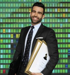 Roy Hage, a handsome Lebanese American opera singer with a modern Arab and Stanford MBA background, smiles confidently in a tailored suit, holding a briefcase and Grammy certificates against a vibrant mosaic backdrop, showcasing his stylish, professional persona.