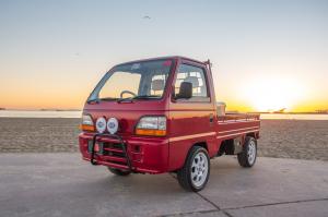 Red Honda Acty Kei truck at sunset with custom front bumper and Hella lights, captured at the beach, representing Oiwa Garage's premium Japanese mini truck enhancements.