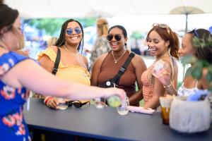 Three woman standing at a bar having wine poured for them