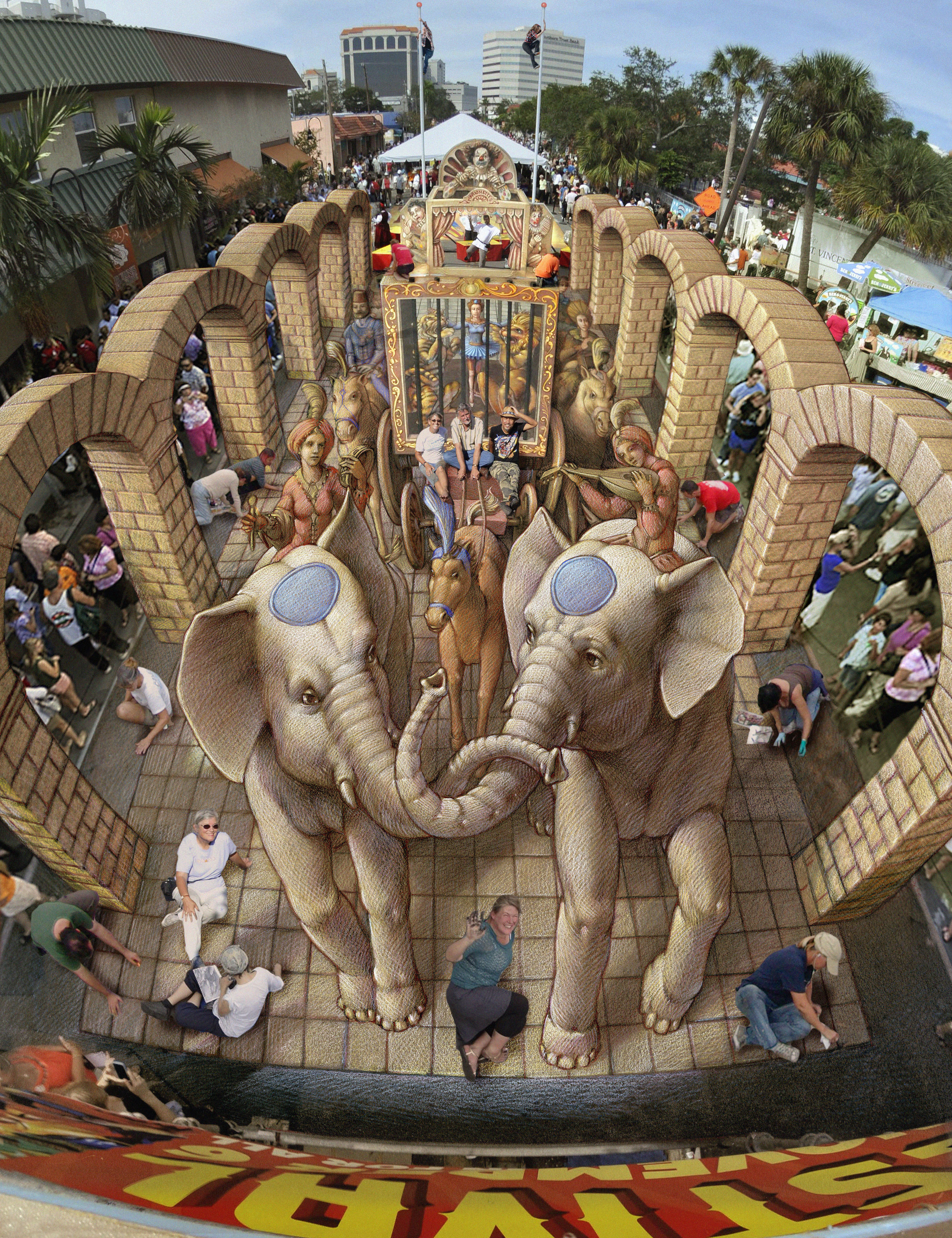 The oversized chalk painting has elephants, lions and tigers with elegant people riding horses. Arches are an added illusion. Artists are sitting on the artwork that is an illusion making the images appear to be 3 dimensional. Nick Wallenda and his wife E