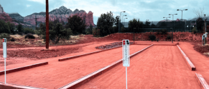 A vibrant red court adorned with a few poles and surrounded by several trees