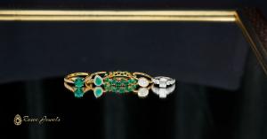 A collection of colored gemstone promise rings including emerald and diamond rings on a reflective surface, presented by Rosec Jewels.