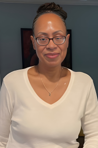 A woman wearing glasses and a white shirt, smiling softly while looking directly at the camera.