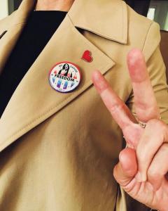 Person flashing a peace sign and wearing a "We Choose Freedom" pin on their lapel.