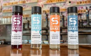 Four sake bottles from Colorado Sake Co on their taproom location bar; a bottle of Blueberry Hibiscus, American Standard, Lychee Nigori and Horchata Nigori.