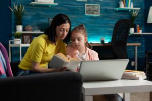 mother-sitting-beside-daughter-holding-school-book-reading-together