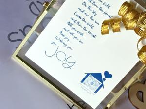 close up of art that sings And Joy song from Smile Songs Holiday Joy collection in gold frame featuring song lyrics and house with heart icon in blue with qr code that sings song when scanned
