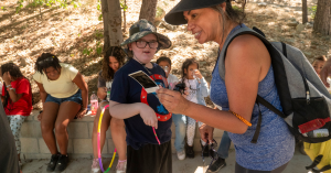 Female camp counselor showing a photograph to a young camper with down syndrome while waiting for an activity to start.