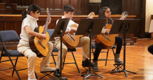 Three young guitarists sit in a row, playing a piece at a concert in Broadway Presbyterian Church