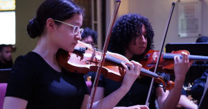 Two violinists play amongst an orchestra of teens and adults at a concert.