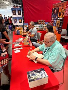 Bestselling authors Orson Scott Card and Hugh Howey seated and signing books at the Galaxy Press booth.