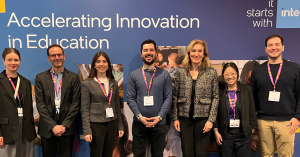 A group photo of the Twin Science team standing alongside members of the Intel Education team in front of a large banner that reads 'Accelerating Innovation in Education.' The seven individuals, all wearing conference badges, are standing in a row and smi