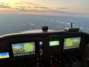 Sunset view from the cockpit of a Cessna 172 TAA, with advanced avionics displays and a scenic horizon.