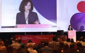 Woman speaking at a conference with people seated in the foreground.