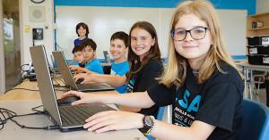 campers sitting at desks with their laptops open learning how to code.