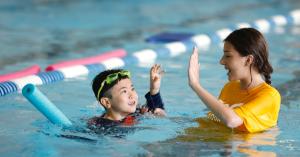 Swim camper being high fived by his instructor in the pool.