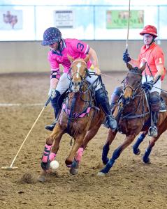 Two arena polo players on horses gallop down the arena