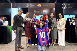 Miembros del equipo del EBC Financial Group y participantes posan juntos en la iFX Expo Asia 2024 en Bangkok, mostrando merchandising compartido con el FC Barcelona. 