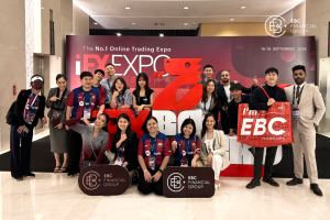 Foto grupal de los miembros del equipo del EBC Financial Group en la iFX Expo Asia 2024 en Bangkok, frente al gran logotipo rojo de la iFX Expo.