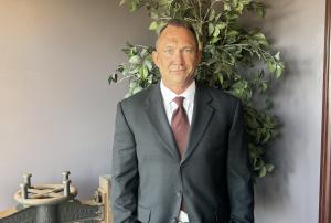 Eric Kaasa standing in charcoal suit with burgundy tie, hair parted at side and side smile