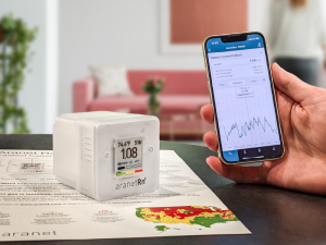 Aranet Radon Plus sensor placed on a radon map of USA and a hand holding a phone with Aranet Home app open.