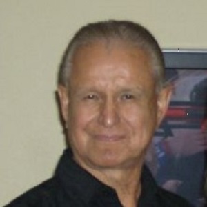 A headshot of George Russell, a Tribal Elder of the Saginaw Chippewa Indian Tribe, smiling in front of a framed picture.