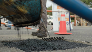 A worker rakes freshly poured carbon-sequestering asphalt into place during a demonstration in Long Island, showcasing the innovative use of solid Modern Carbon from methane pyrolysis in road construction. The asphalt mixture is spread to demonstrate its 