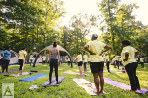 Group Yoga Retreat, women outdoors with yoga mats and tents surrounding them under trees