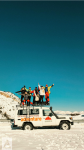 Blue sky, group of people on top of an adventure land rover in the snow
