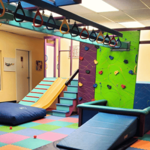 A brightly colored therapy room featuring a slide, climbing wall, padded mats, and hanging rings for physical activities.