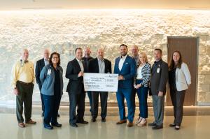 Group of business professionals and healthcare professionals smiling with a large check from DOCUmation, being presented to University Health Foundation.