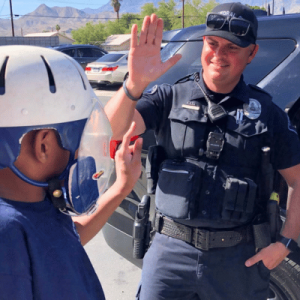 A child in a helmet high-fiving a uniformed police officer outdoors.