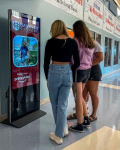 Three High Schoo students curiously engage with a NextGrad Digital Out of Home Screen in a High School.