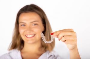 A smiling young woman proudly displays her clear aligner, which has effectively straightened her teeth.