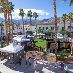 white-walled portable tents on a lawn, artwork, people walking around, surrounded by Old World Spanish Colonial Architecture