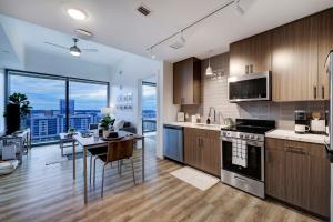 Modern kitchen with wooden cabinetry and stainless steel appliances, adjacent to an open-plan dining and living area with large windows offering a scenic view of the city skyline