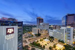 Night view of a city skyline with a Texas A&M EnMed building prominently featured, and surrounding high-rise buildings illuminated against the evening sky