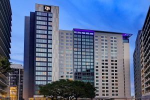 Exterior view of a modern high-rise building with Texas A&M branding, featuring sleek architecture and illuminated windows at dusk