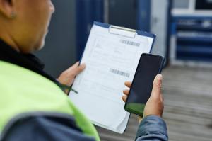 A close-up of a worker holding a clipboard while entering data on a mobile phone.